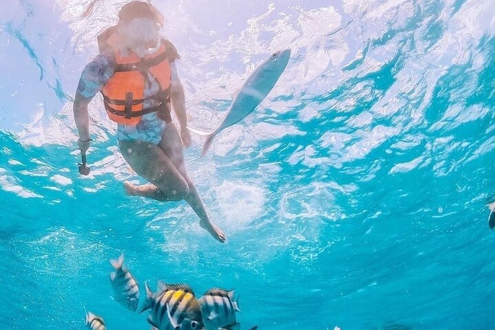 Snorkelers swimming near the arches of Los Arcos with boats floating in the clear blue water.